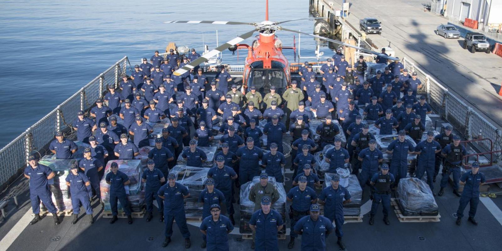 United States Coast Guard at attention on deck of rescue vessel with USCG helicopter