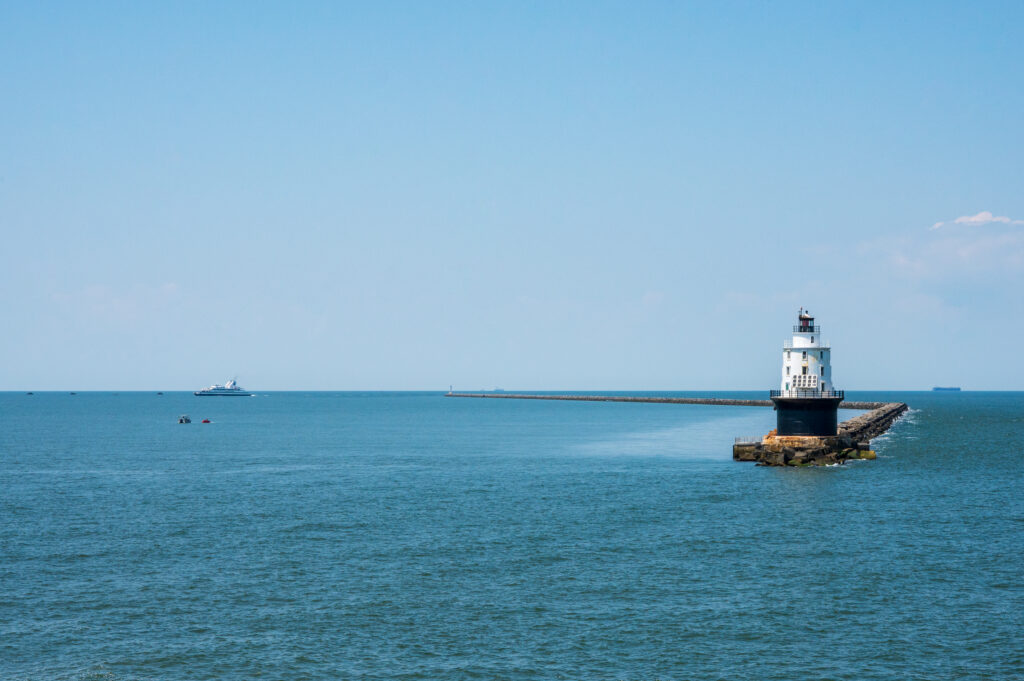 Wide shot photo of the Harbor of Refuge Lighthouse with the Cape-May Lewes Ferry Sailing in the background.