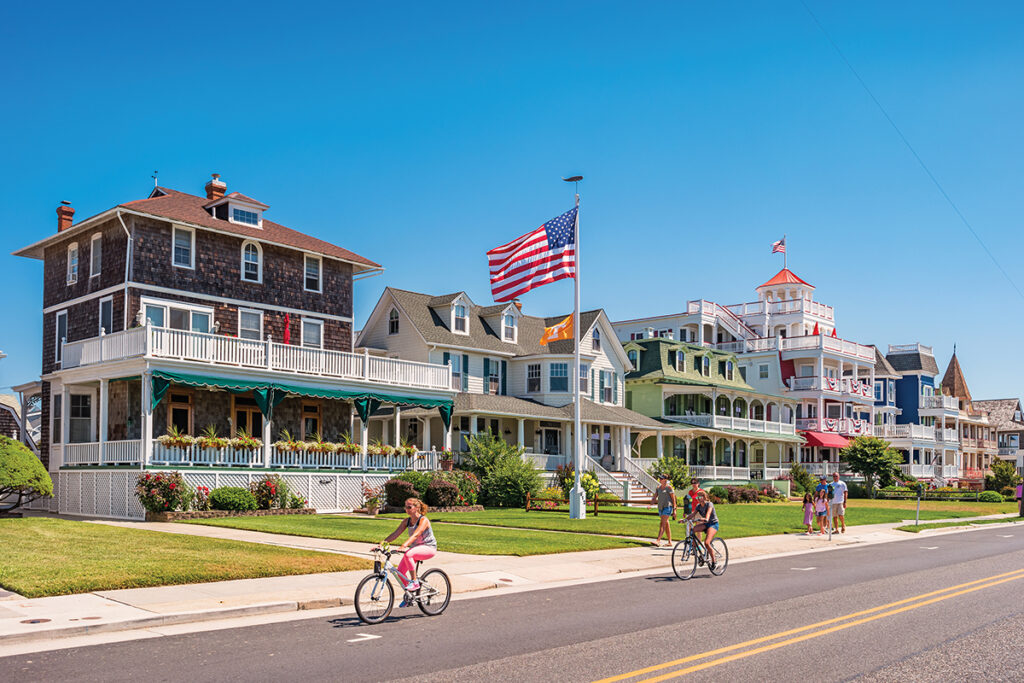 People bike and walk in front of traditional villas in Cape May, New Jersey, USA, on a sunny summer day
