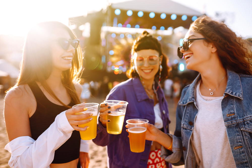 Three girls at a beach festival toasting their drinks