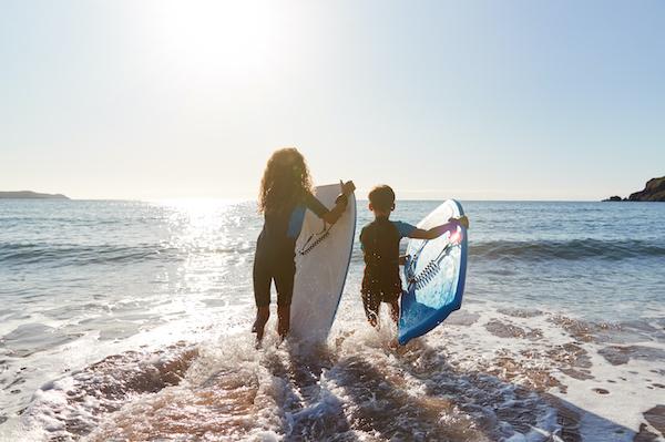 Two children stepping into the ocean holding boogie boards.