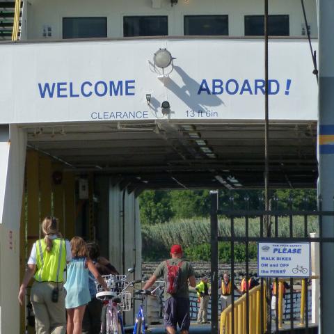 Cape May-Lewes Ferry boarding process, showing foot passengers and cyclists entering the car deck under the 13'6" clearance sign, emphasizing safe travel and size restrictions.