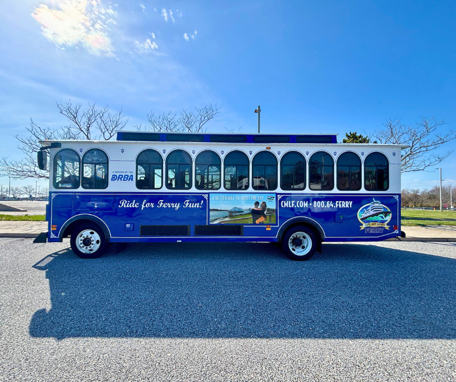 A side view of the shuttle (or trolley) belonging to the Cape May - Lewes Ferry. Creme and blue paint with the CMLF and DRBA logos