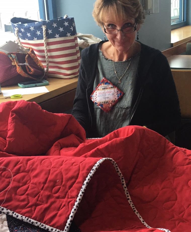 Quilts of Valor volunteer works finishing touches on a red quilt.