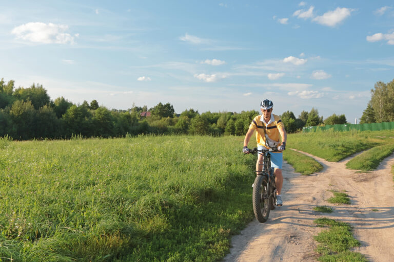 Cyclist in helmet with equipment on electric bicycle rides along path in field in Cape May County NJ