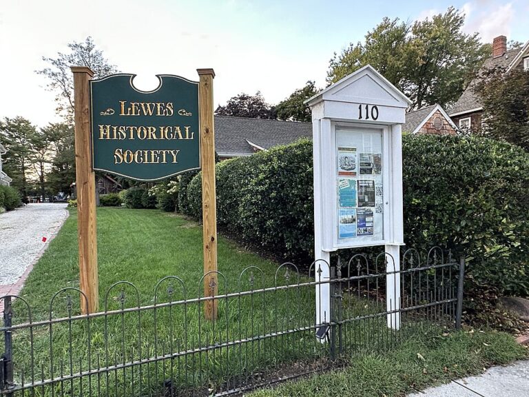 The Lewes Historical Society wooden sign beside a white outdoor bulletin board display at the entrance to the Shipcarpenter Street campus. Photo by Nolabob (https://commons.wikimedia.org/wiki/File:LHSShipcarpenterCampus.jpg) , CC BY-SA 4.0 (https://creativecommons.org/licenses/by-sa/4.0) , via Wikimedia Commons.