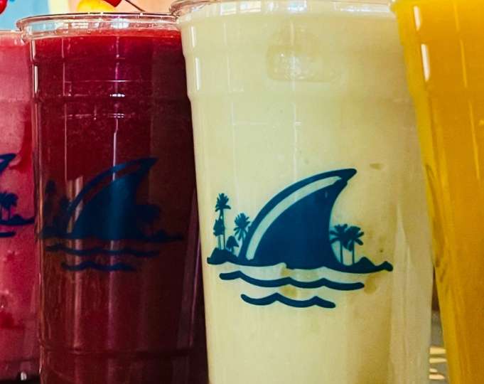 A few colorful tropical cocktail drinks in branded glasses with shark fins.