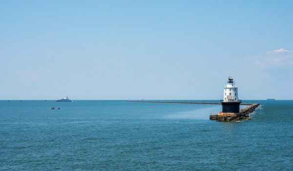 Wide shot photo of the Harbor of Refuge Lighthouse with the Cape-May Lewes Ferry Sailing in the background.