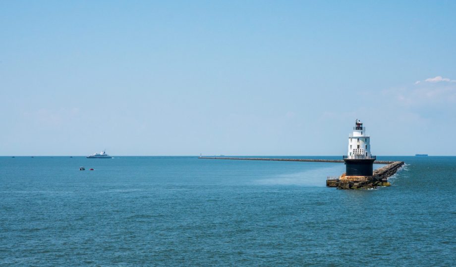 Wide shot photo of the Harbor of Refuge Lighthouse with the Cape-May Lewes Ferry Sailing in the background.