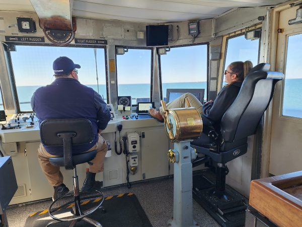 A photo of Captain Palmer and the Pilot in the wheelhouse while the Ferry crosses Delaware Bay on a bright sunny day