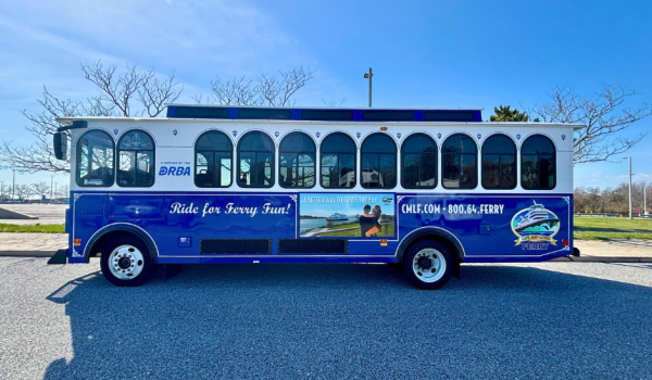 A side view of the shuttle (or trolley) belonging to the Cape May - Lewes Ferry. Creme and blue paint with the CMLF and DRBA logos