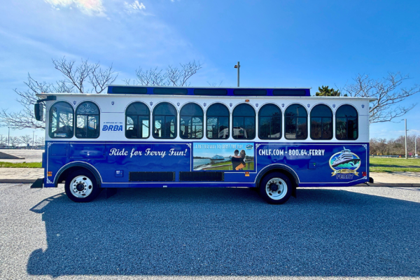 A side view of the shuttle (or trolley) belonging to the Cape May - Lewes Ferry. Creme and blue paint with the CMLF and DRBA logos