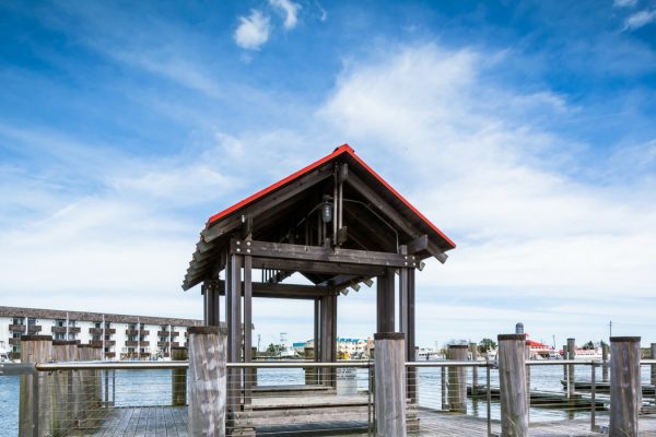 Panoramic shot of the wooden pier and covered gazebo at a Cape May-Lewes Ferry terminal, highlighting the scenic Delaware Bay view under a bright blue sky.