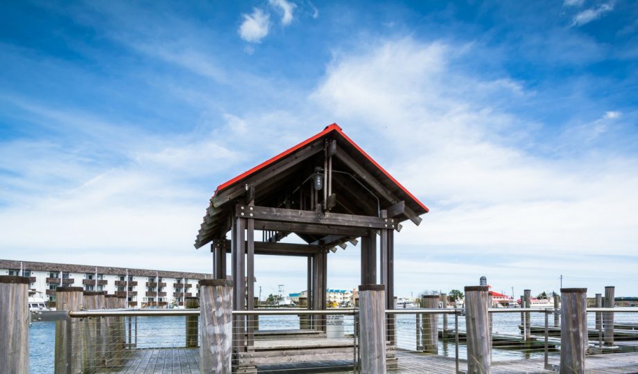 Panoramic shot of the wooden pier and covered gazebo at a Cape May-Lewes Ferry terminal, highlighting the scenic Delaware Bay view under a bright blue sky.