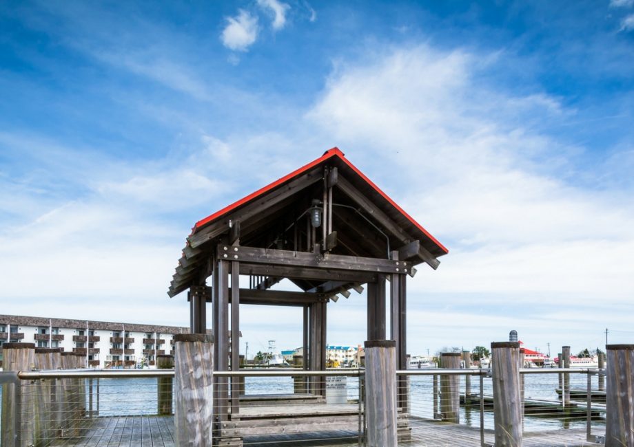 Panoramic shot of the wooden pier and covered gazebo at a Cape May-Lewes Ferry terminal, highlighting the scenic Delaware Bay view under a bright blue sky.